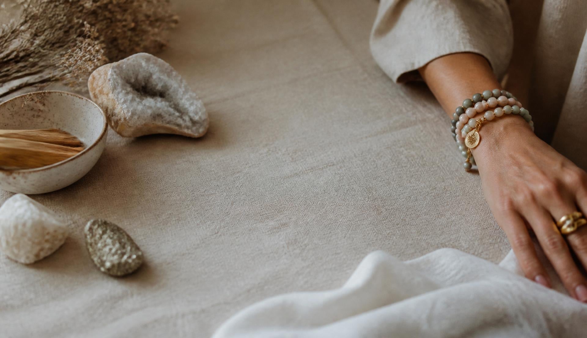 A wrist wearing natural gemstone bead bracelets resting on linen beside raw mineral pieces
